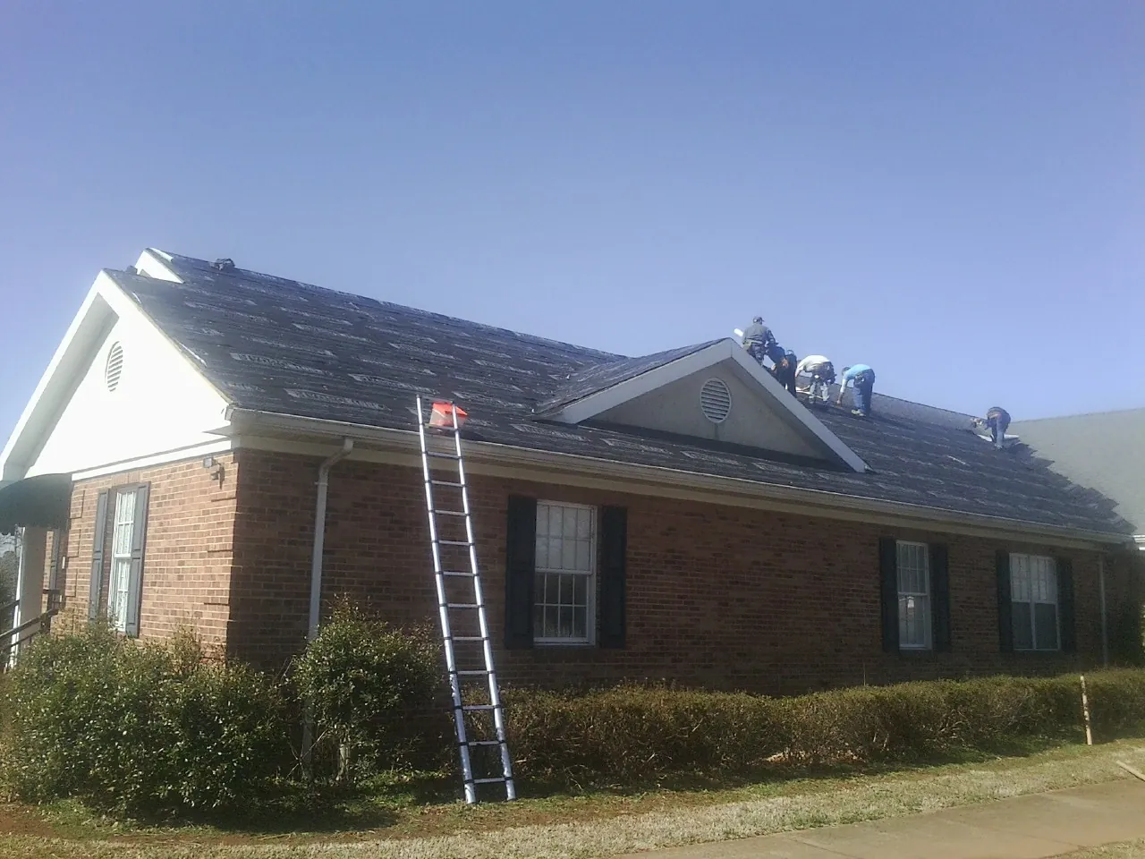 Crew tearing shingles off a brick ranch roof with a ladder set — Emergency Roof Repair work by our crew in Pelican Rapids