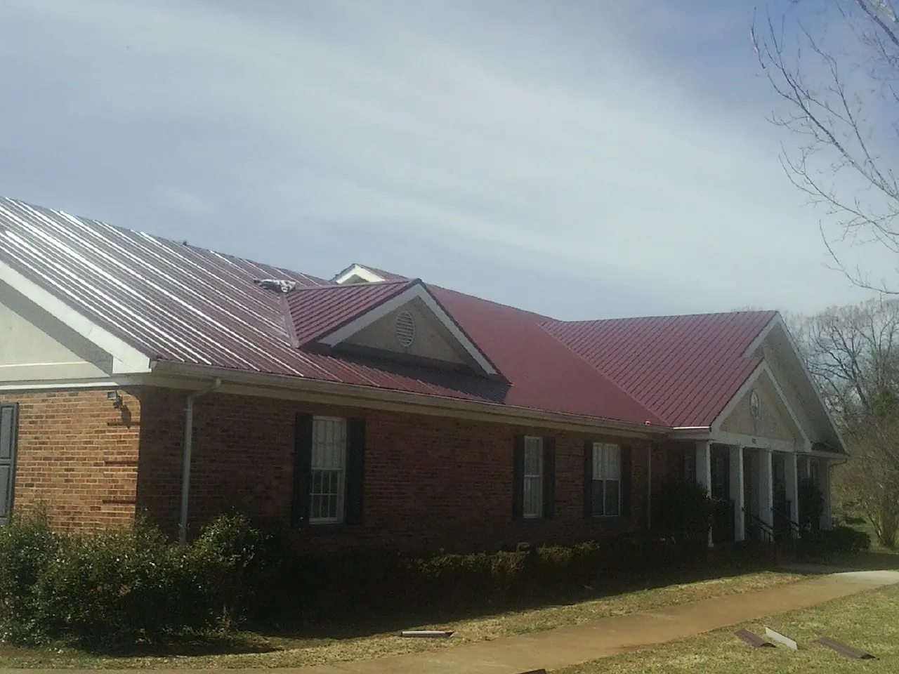 Red metal roof with gabled entries on a long brick building, from a Hail Damage Roof Repair job in Pelican Rapids
