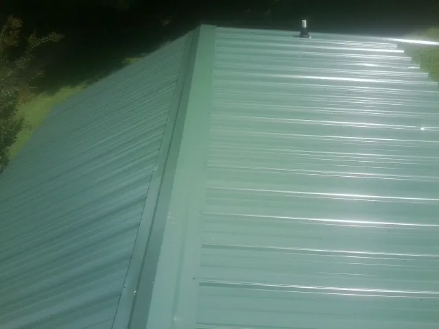 New green metal panels meeting at the ridge of a roof — Flat Roof Repair work by our crew in Pelican Rapids