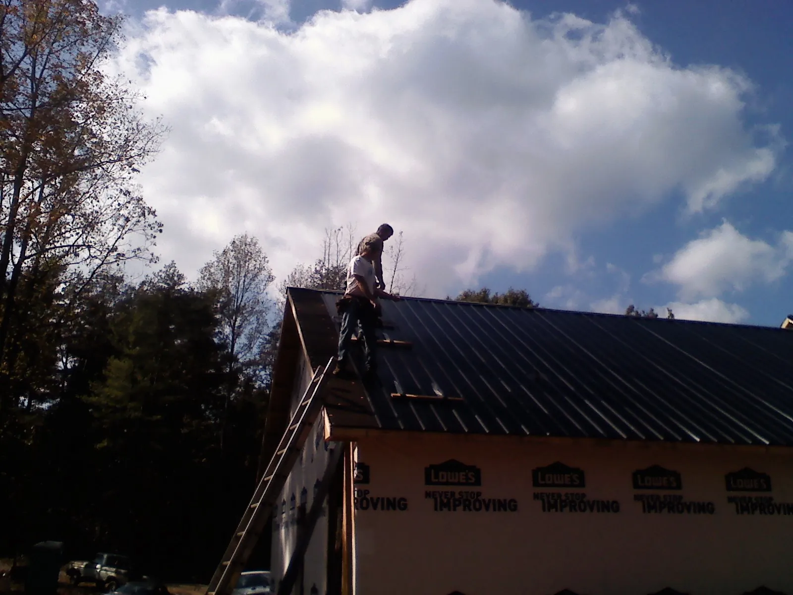 Roofer fastening dark metal panels high against a cloudy sky, from a Roof Inspection job in Pelican Rapids