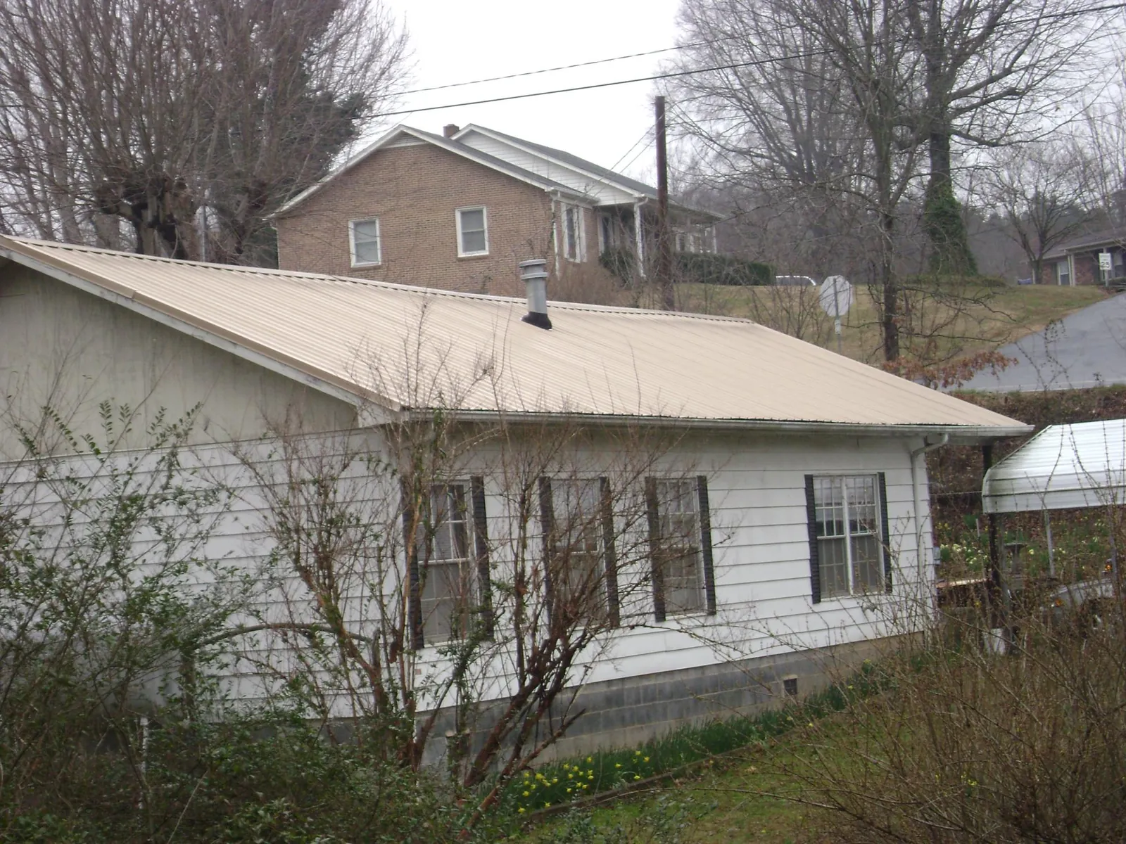 Tan metal roof on a white sided house set into a hillside — Commercial Roofing by Roofing Brothers in Pelican Rapids